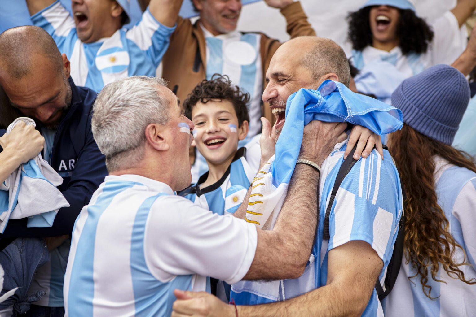 Medium shot of Argentinian football fan friendd and little boy celebrating goal while standing in the crowd at stadium
